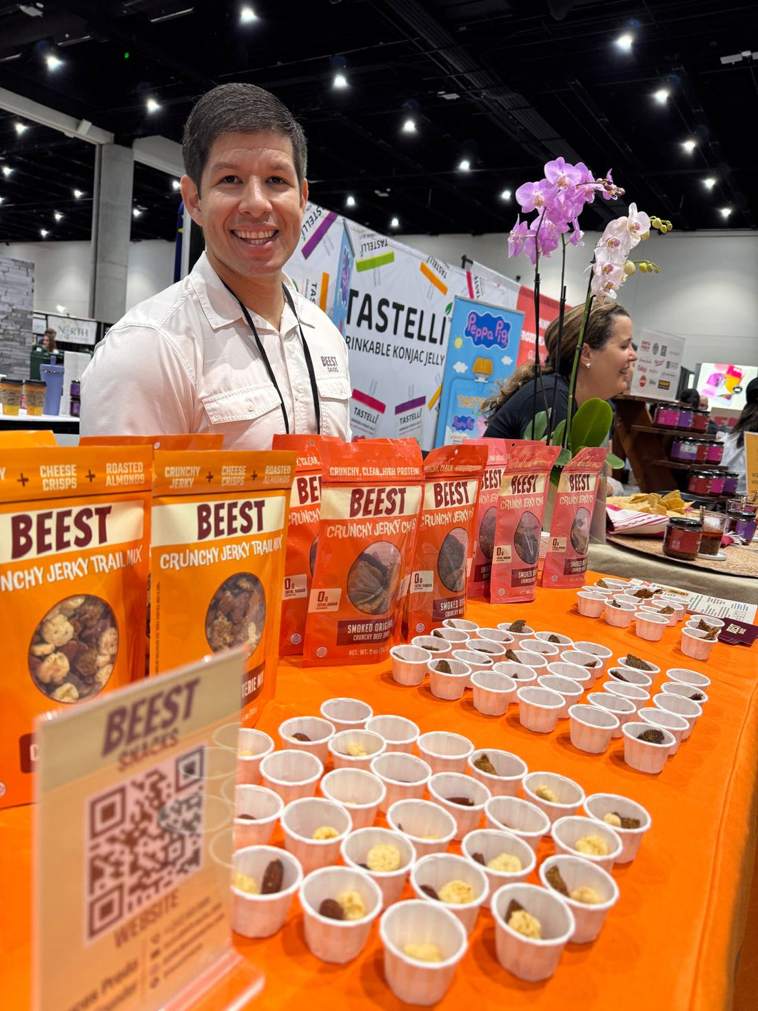 BEEST Snacks booth at a trade show with a smiling representative behind a table displaying Crunchy Jerky Chips product packaging and samples.