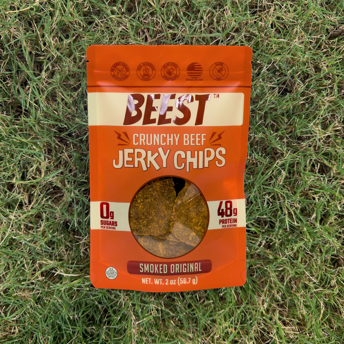 A 2 oz bag of BEEST Beef Jerky Chips, Smoked Original, lying on green grass