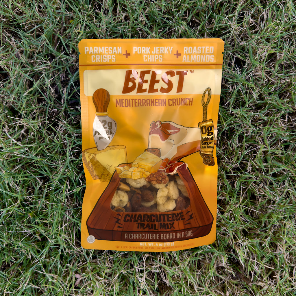 A 4 oz bag of BEEST Charcuterie Trail Mix, Mediterranean Crunch, lying on green grass