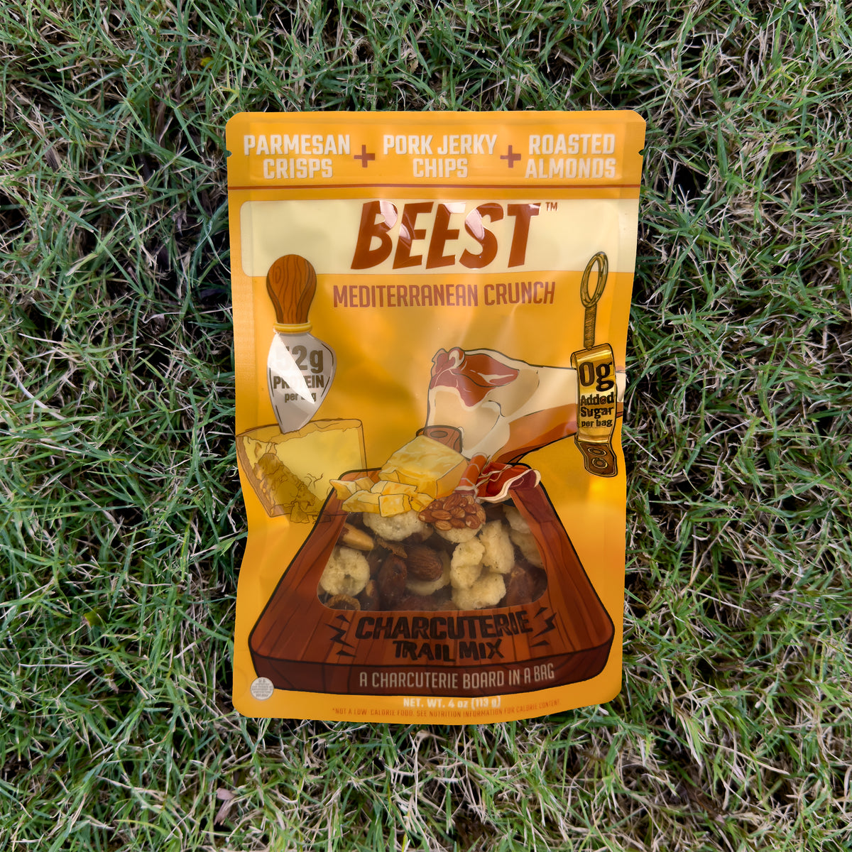A 4 oz bag of BEEST Charcuterie Trail Mix, Mediterranean Crunch, lying on green grass