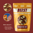 Graphic with BEEST Charcuterie Trail Mix on red background showing 2 oz bag with close-up circles and callouts describing 52g of protein and real ingredients; high-protein clean snack. And a picture of the bag being carried on a hike.