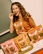 Woman holding a package of 'BEEST' Beef Jerky Chips and about to bite into a jerky chip in an indoor setting
