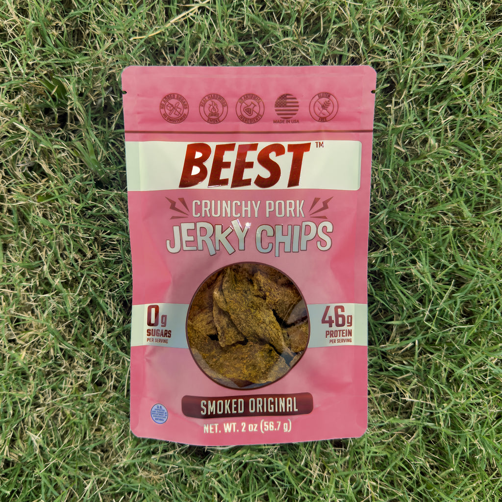 A 2 oz bag of BEEST Pork Jerky Chips, Smoked Original, lying on green grass
